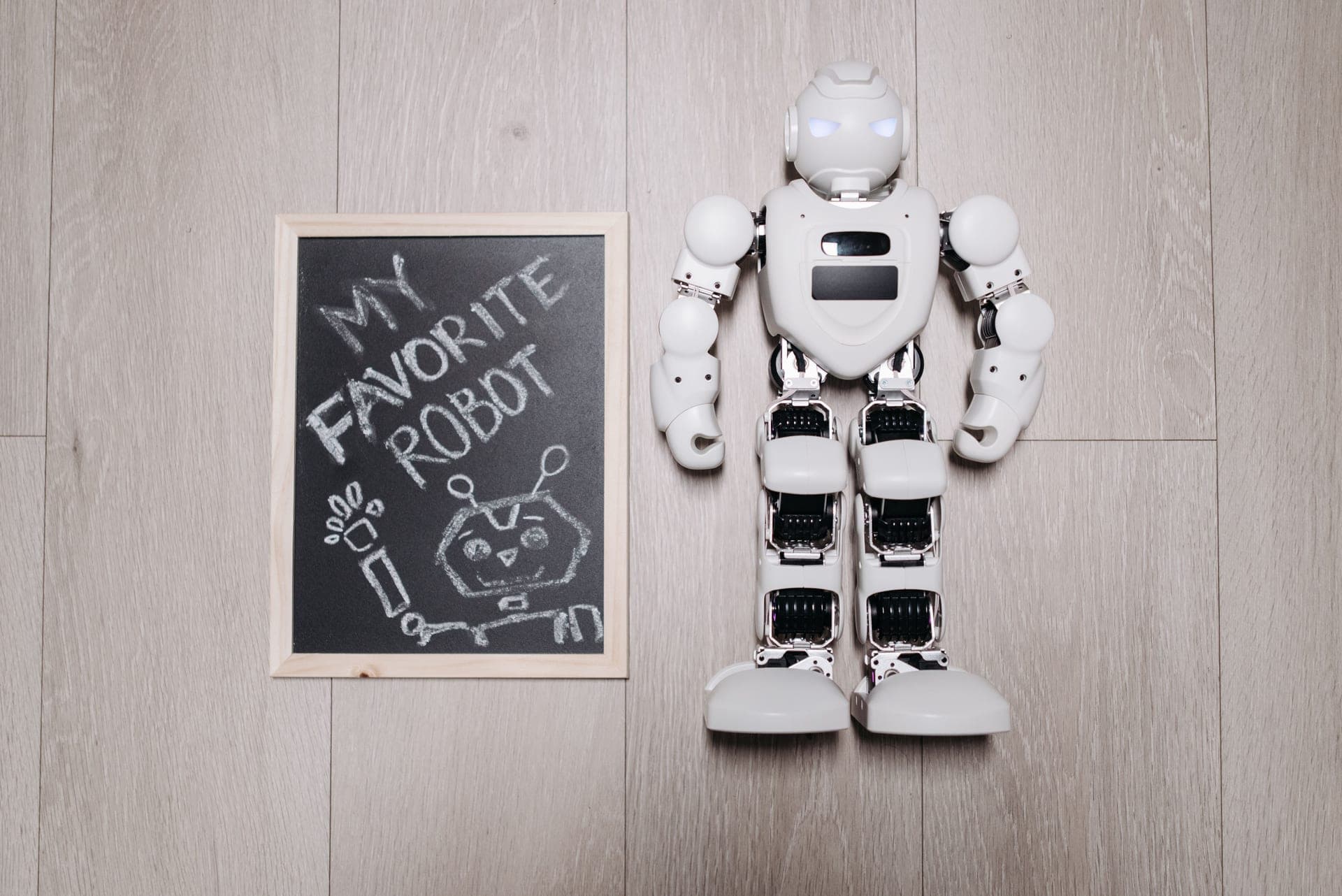 A toy robot beside a chalkboard drawing on a wooden floor